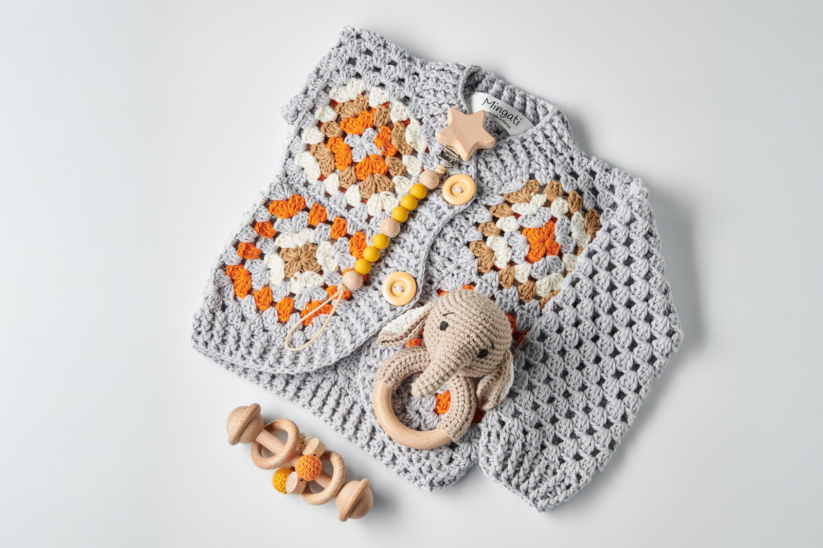 Baby Cardigan aus Baumwolle in Handarbeit gehäkelt in Grau mit Muster, kombiniert mit Holzgreifling und Rassel